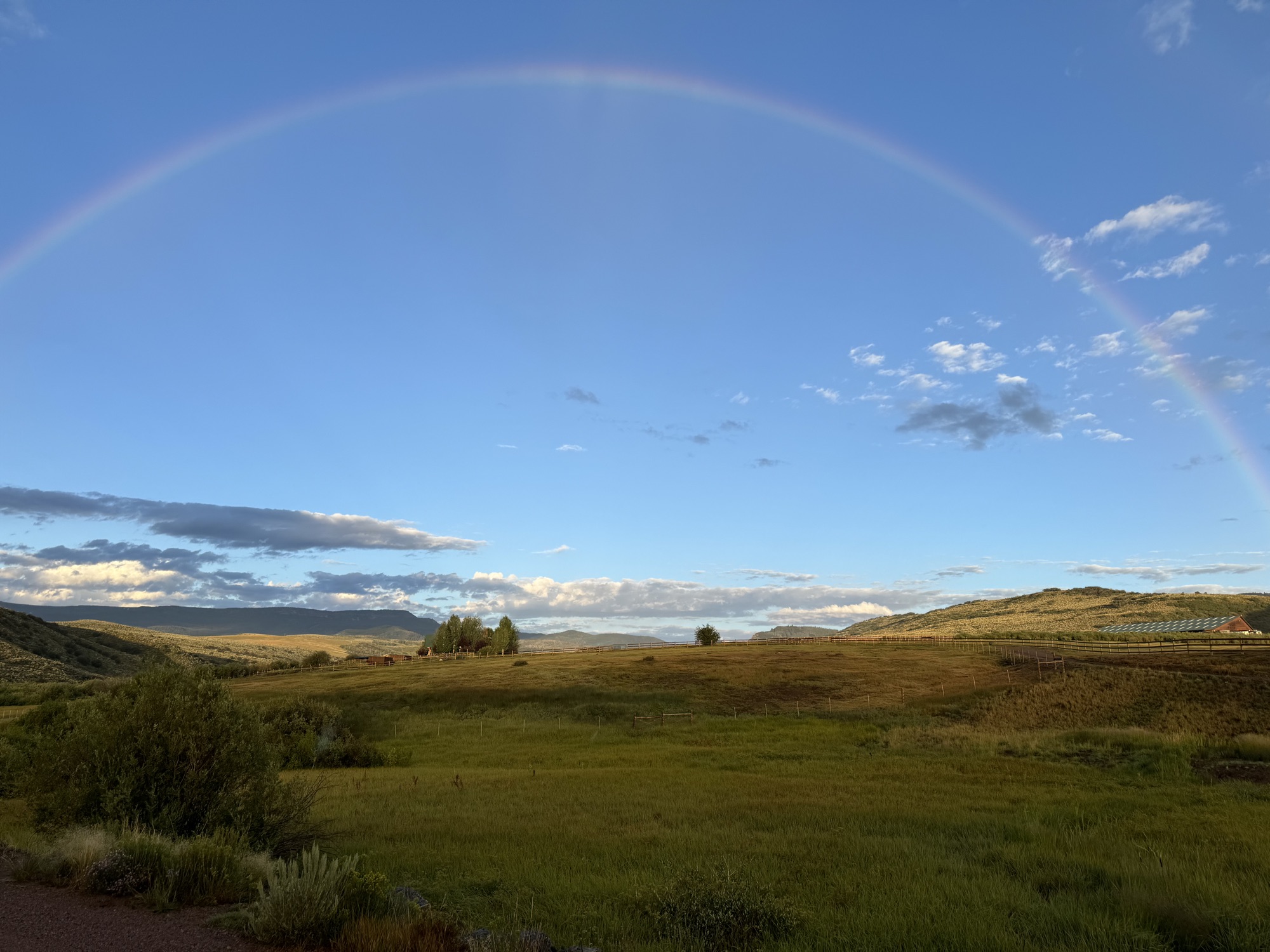 A rainbow over open pasture, sage hills and a barn at the ranch