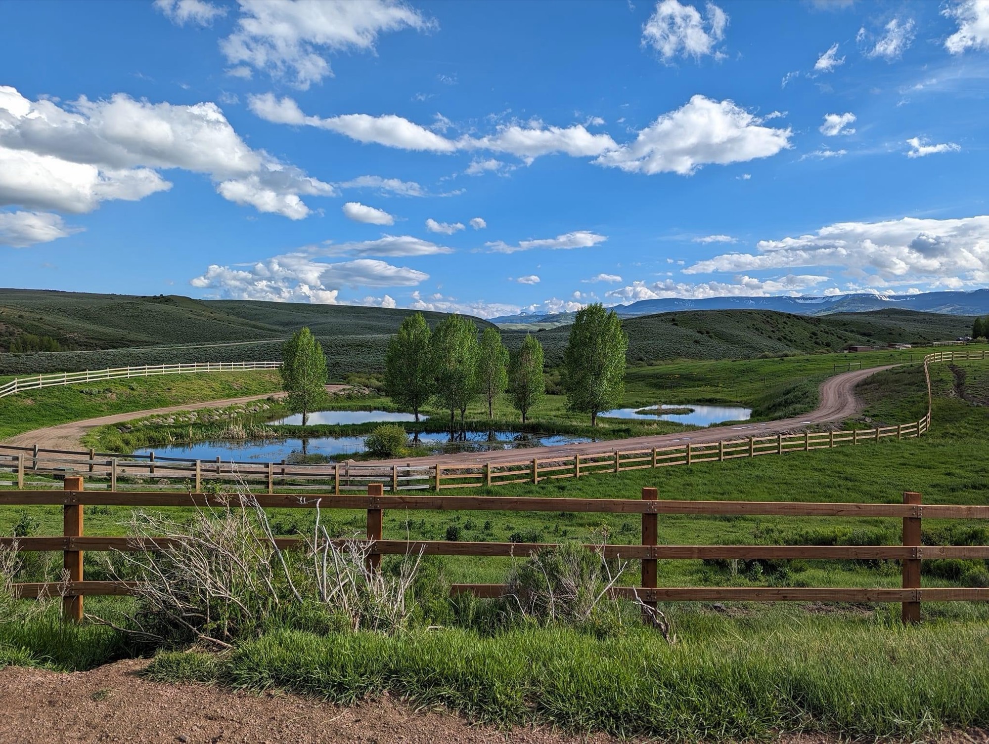 Ponds ringed by aspens and wood rail fences, with rolling hills and mountains beyond